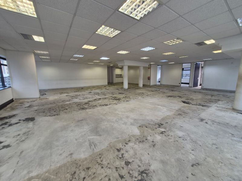 A large, open-plan office space featuring a suspended ceiling with recessed lighting and structural columns, currently requiring new flooring installation.