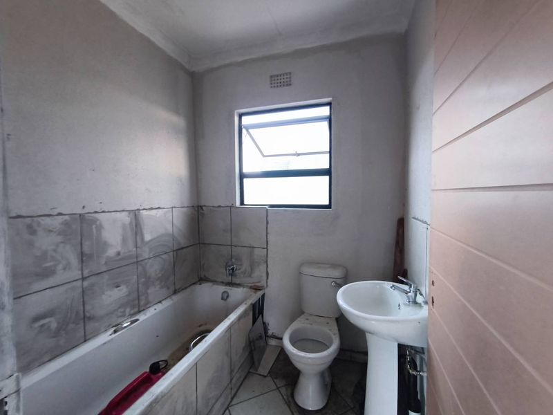 A bathroom in need of renovation, featuring a bathtub, pedestal sink, and toilet, with unfinished wall surfaces and incomplete tiling.