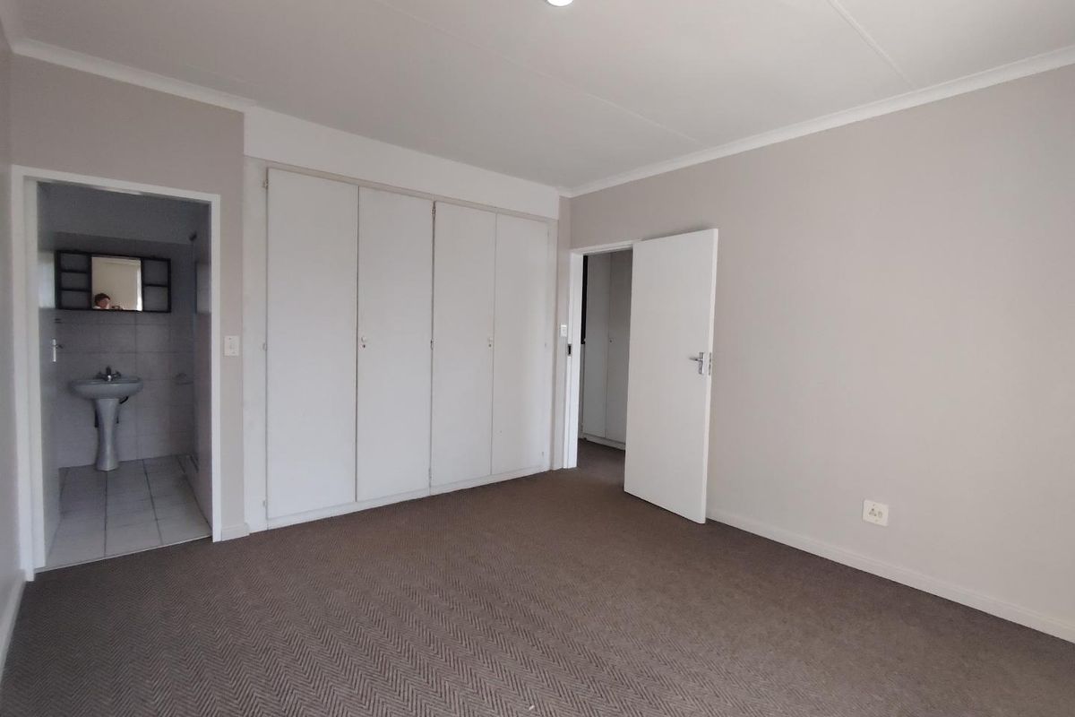 Spacious bedroom featuring neutral carpeting, built-in cupboards, and direct access to an en-suite bathroom.