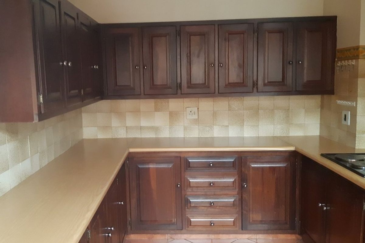 A functional kitchen featuring dark wood cabinetry, laminate countertops, and a tiled backsplash, offering a classic layout ready for modern updates.