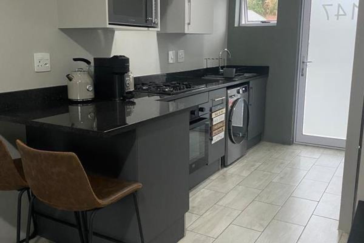 Modern kitchen featuring dark cabinetry, granite countertops, built-in oven, gas hob, and integrated laundry appliances with direct access to the exterior.