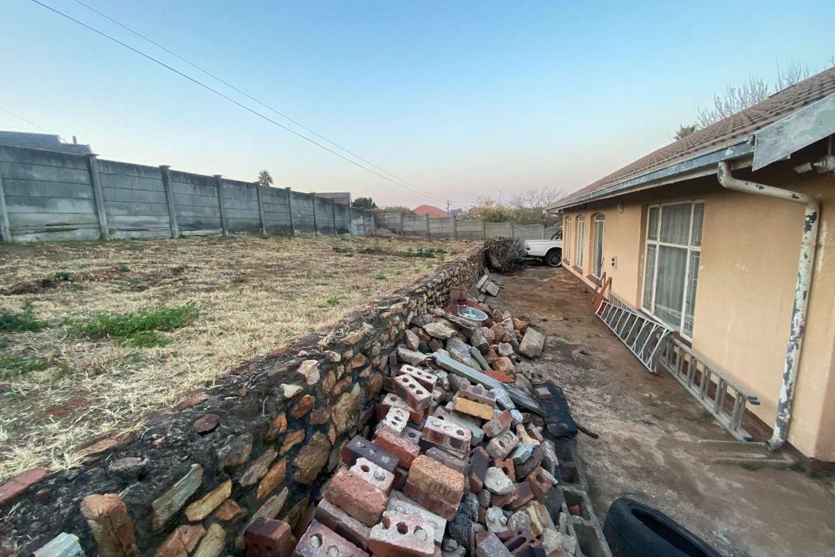 Rear exterior view of the property showing a large unmaintained garden area, stone retaining wall, and significant accumulation of construction debris.