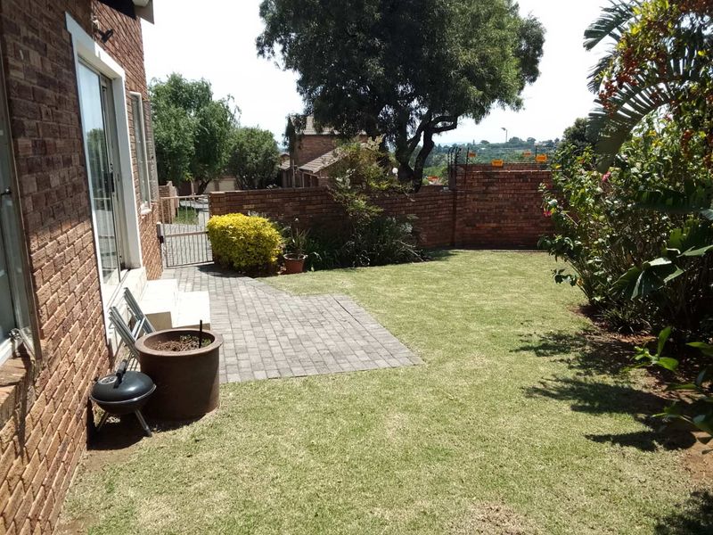 A private rear garden featuring a paved patio area, established lawn, and brick boundary walls, accessible via a sliding glass door.