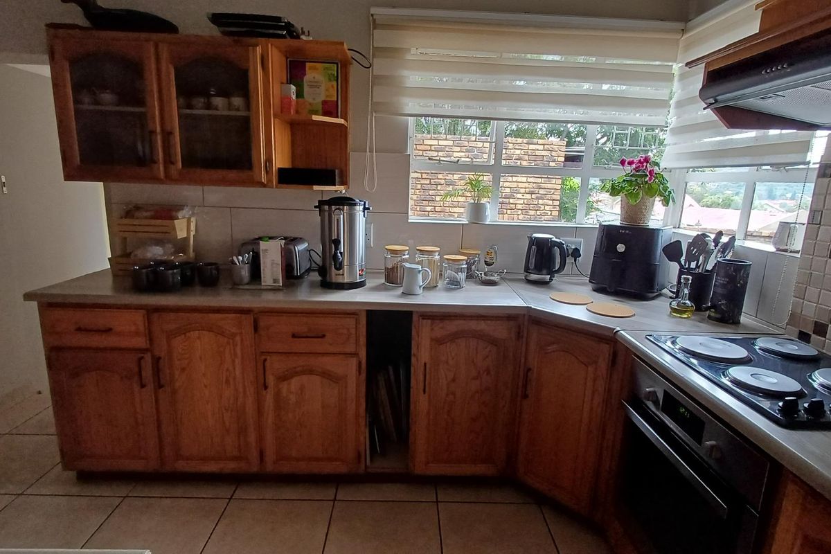 A functional kitchen featuring timber cabinetry, tiled splashbacks, a built-in oven, and a ceramic hob, offering a practical layout for daily meal preparation.