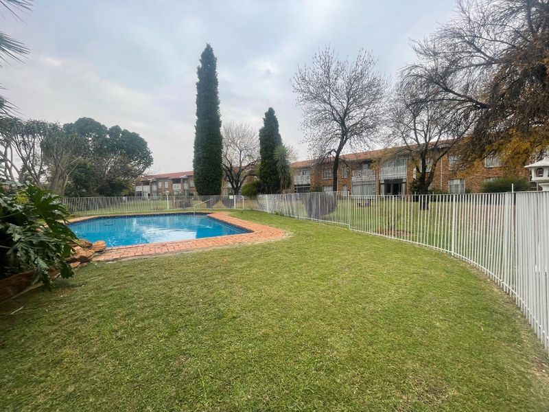 Communal outdoor area featuring a swimming pool with brick coping, surrounded by a manicured lawn and secure metal perimeter fencing.
