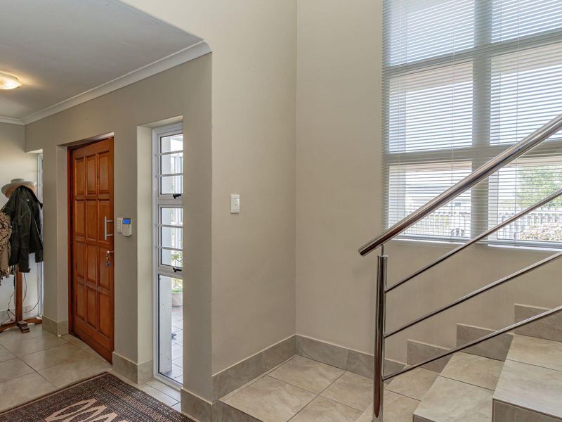 A bright and spacious entrance hall featuring tiled flooring, a modern stainless steel balustrade, and a solid timber front door.