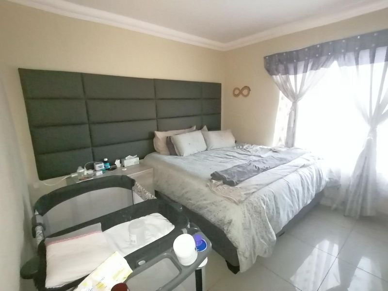 A bedroom featuring a large upholstered headboard, tiled flooring, and natural light from the window.