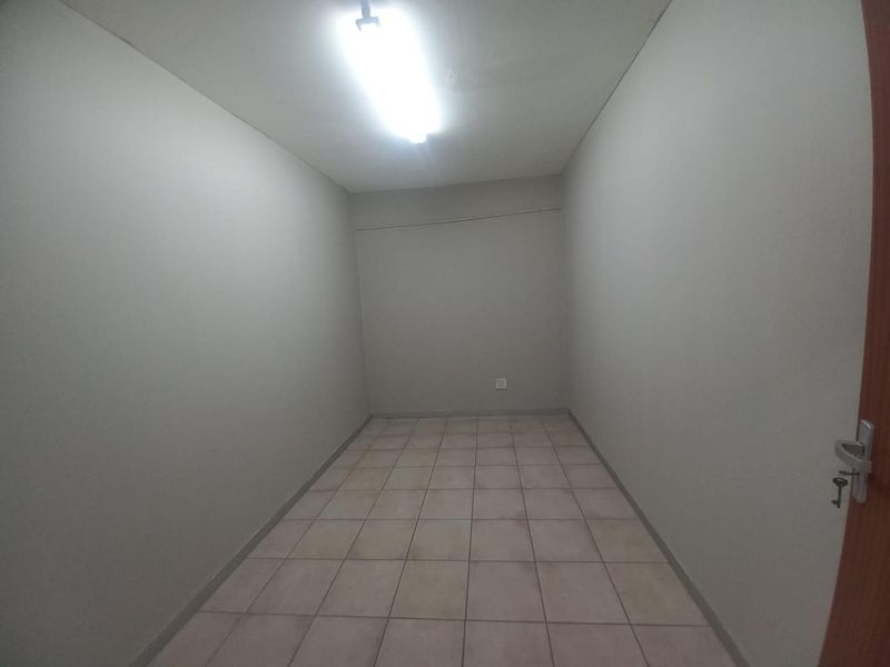 A vacant, neutral-toned office space featuring ceramic tiled flooring and overhead fluorescent lighting, suitable for a variety of business or administrative uses.
