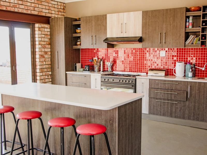 Modern kitchen featuring a central island, two-tone cabinetry, a vibrant red tiled backsplash, and an exposed brick feature wall with access to the outdoors.