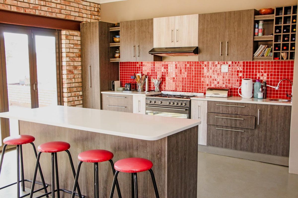 Modern kitchen featuring a central island, two-tone cabinetry, a vibrant red tiled backsplash, and an exposed brick feature wall with access to the outdoors.