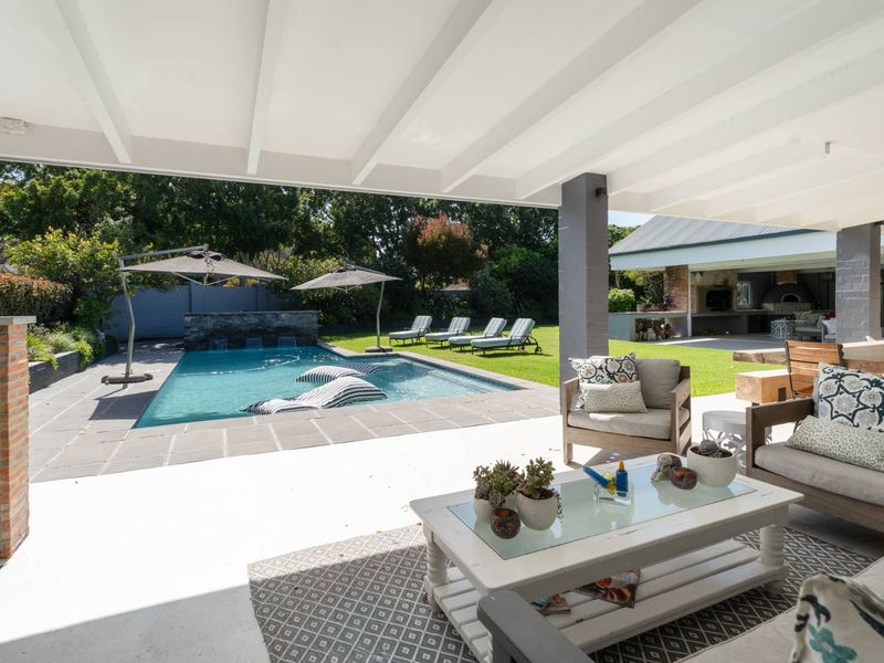 Spacious covered patio overlooking a well-maintained swimming pool, stone water feature, and landscaped garden, perfect for outdoor entertaining.
