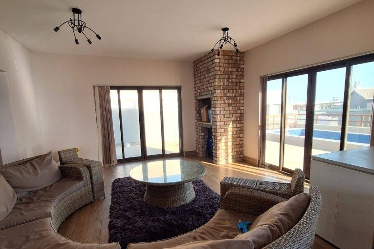 Spacious living area featuring a brick fireplace, wood-look flooring, and large sliding glass doors providing access to the outdoor pool area.