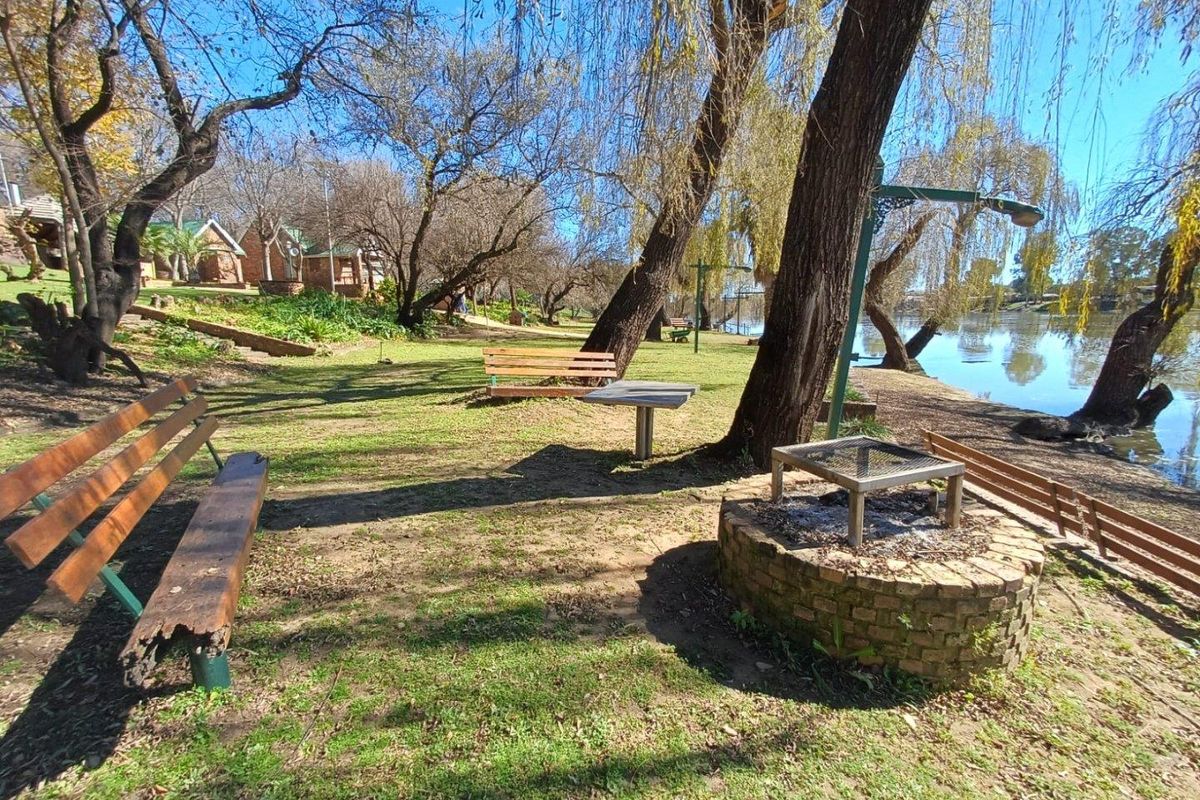 Riverside outdoor recreational area featuring a built-in brick braai, established trees, and scenic water views.