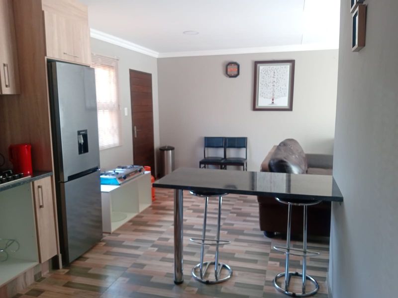 Open-plan living area featuring a kitchen with built-in cabinetry, a breakfast bar, and laminate flooring, seamlessly connecting to the lounge space.