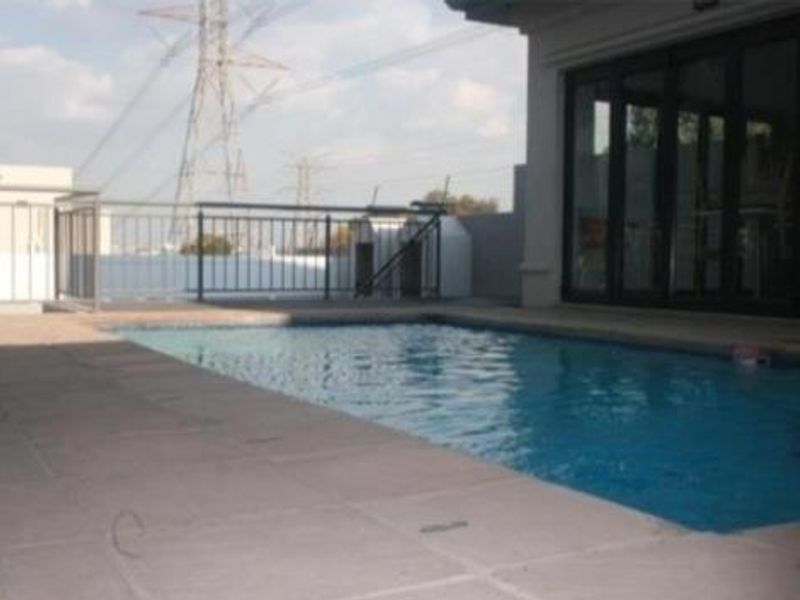 Outdoor swimming pool area featuring a tiled deck, metal safety balustrade, and direct access to the interior via large bi-fold glass doors.