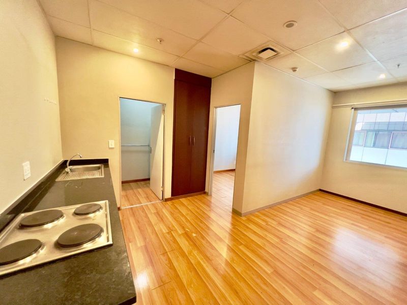Open plan living area featuring laminate flooring, a compact kitchenette with electric hob and sink, and a built-in storage cupboard.