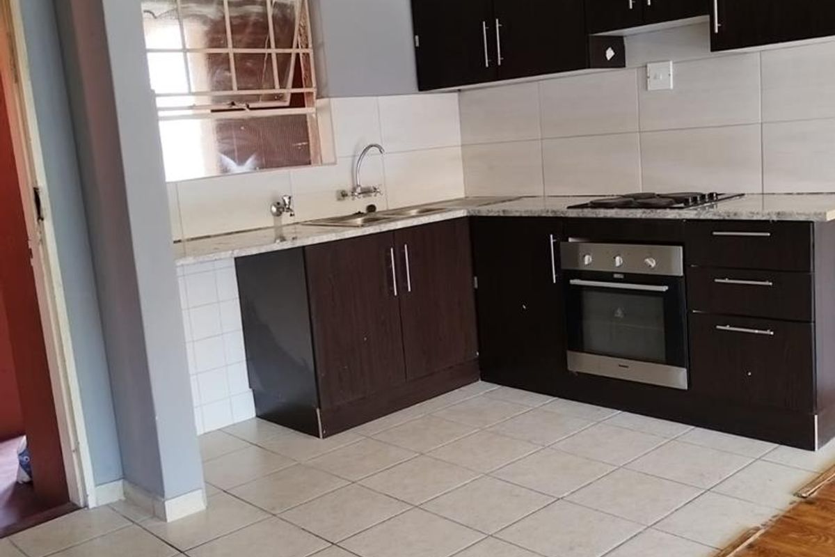 A functional kitchen featuring dark wood cabinetry, granite countertops, built-in oven, gas hob, and tiled flooring, offering a clean and practical workspace.