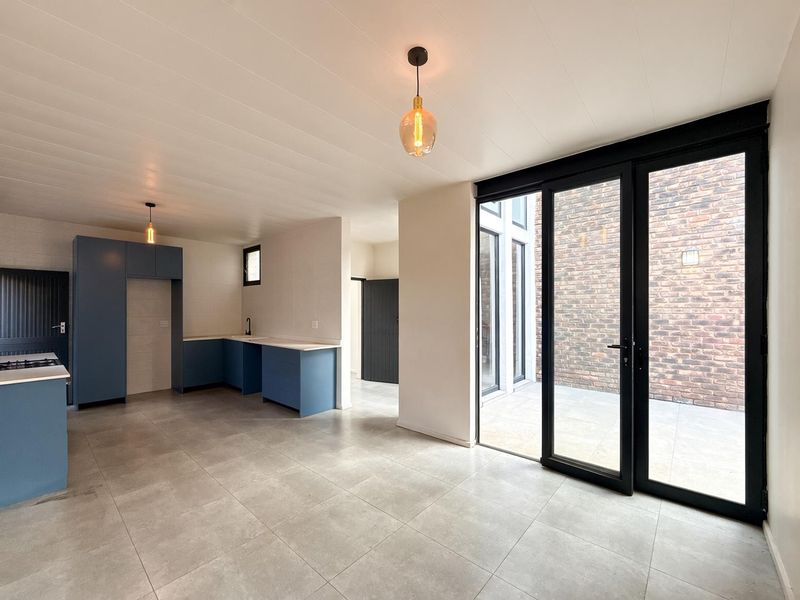 Modern open-plan kitchen and living area featuring blue cabinetry, gas hob, tiled floors, and large sliding doors opening to a private brick-walled courtyard.