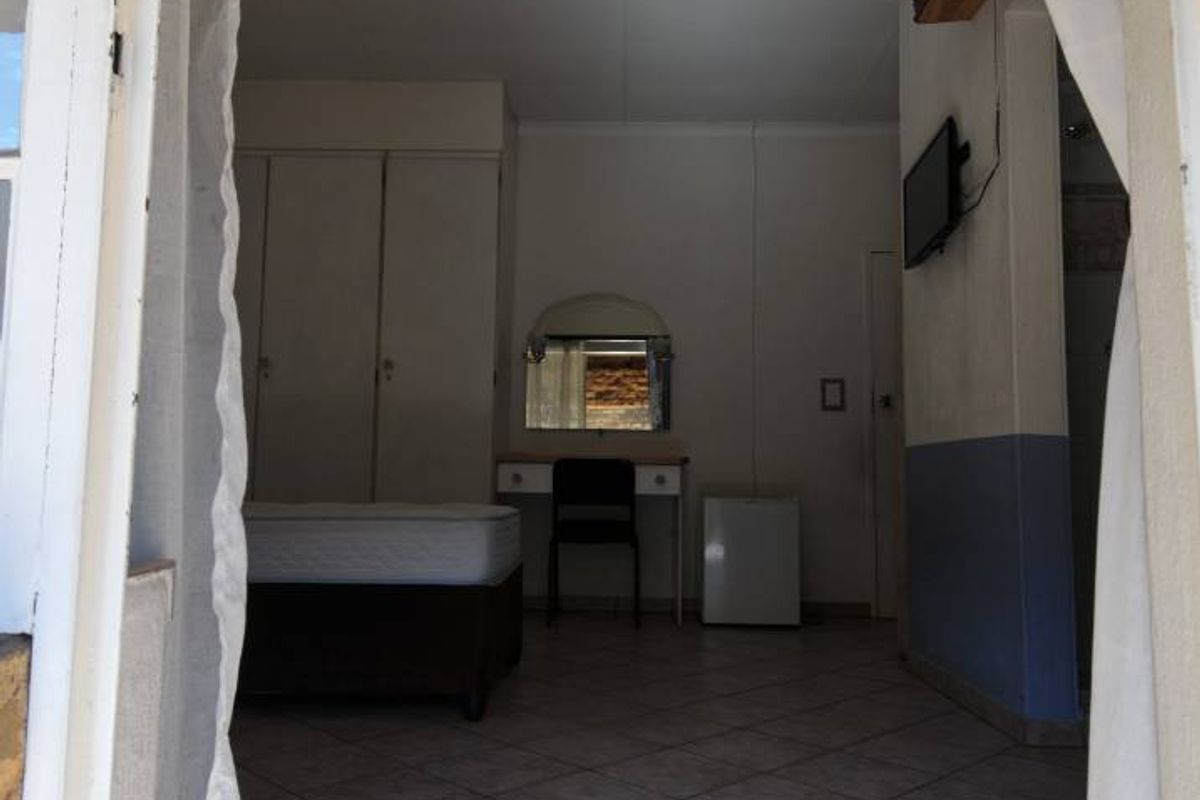 A bedroom featuring built-in cupboards and tiled flooring, viewed from an adjacent doorway.