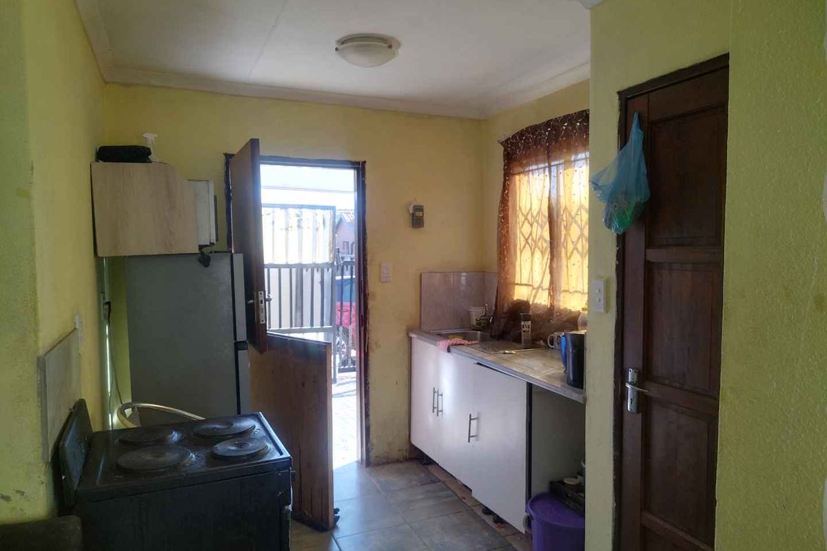 A compact kitchen featuring basic cabinetry, a sink, and a freestanding stove, with direct access to the exterior.