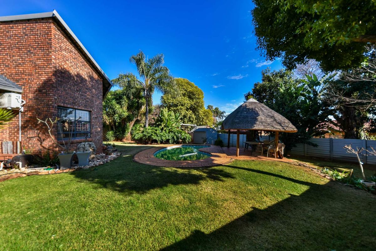Spacious rear garden featuring a swimming pool, a traditional thatch lapa, and established landscaping, providing a private outdoor entertainment area.