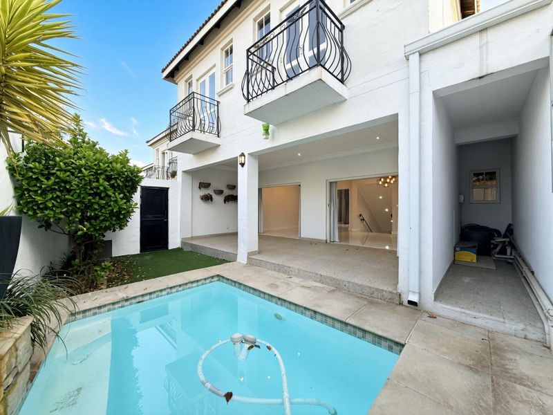 Rear exterior view featuring a swimming pool, covered patio area, and upper-level balconies with wrought iron railings.