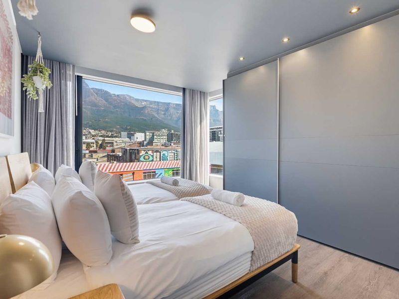 Modern bedroom featuring built-in wardrobes, recessed lighting, and large windows offering scenic mountain and city views.