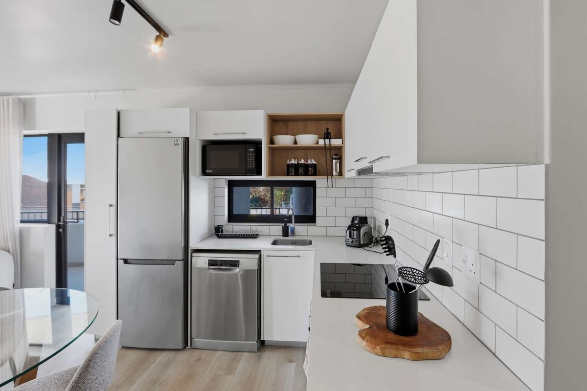 Modern kitchen featuring white cabinetry, subway tile backsplash, integrated sink, and built-in cooktop, seamlessly connected to the living area.