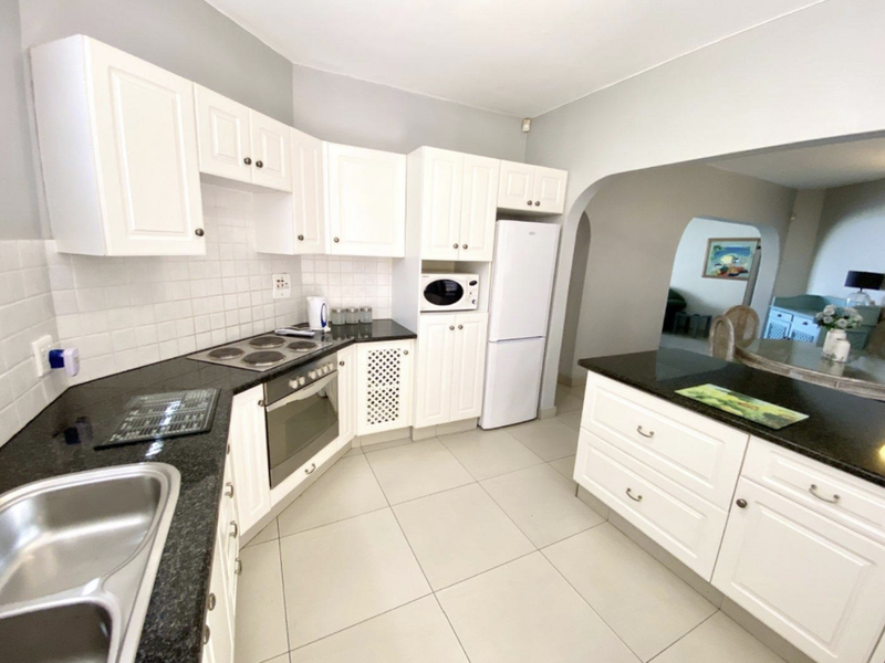 A well-maintained kitchen featuring white cabinetry, dark granite countertops, a built-in oven and hob, and a functional breakfast island.