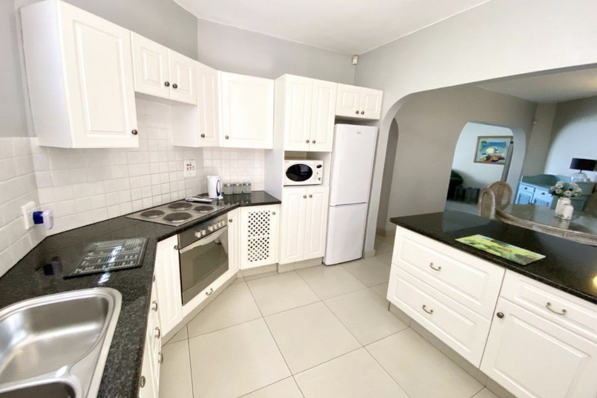 A well-maintained kitchen featuring white cabinetry, dark granite countertops, a built-in oven and hob, and a functional breakfast island.