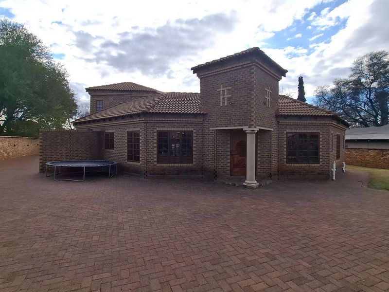 A well-maintained face-brick house featuring a tiled roof, a paved driveway, and a classic columned entrance.