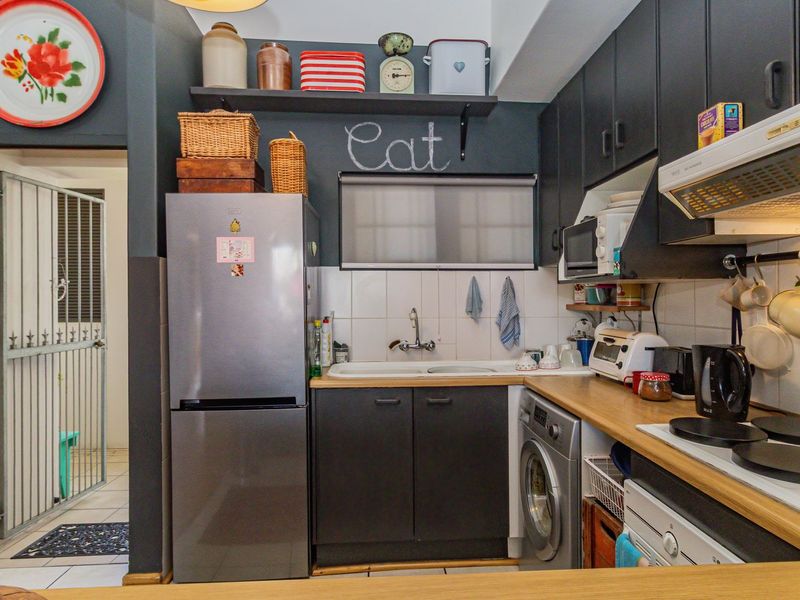 Compact kitchen featuring dark cabinetry, wood-look countertops, tiled backsplash, integrated extractor fan, and built-in shelving, providing a functional and efficient cooking space.