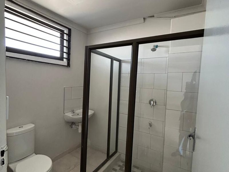 A functional bathroom featuring a shower enclosure, wall-mounted basin, and toilet with neutral tiled finishes.