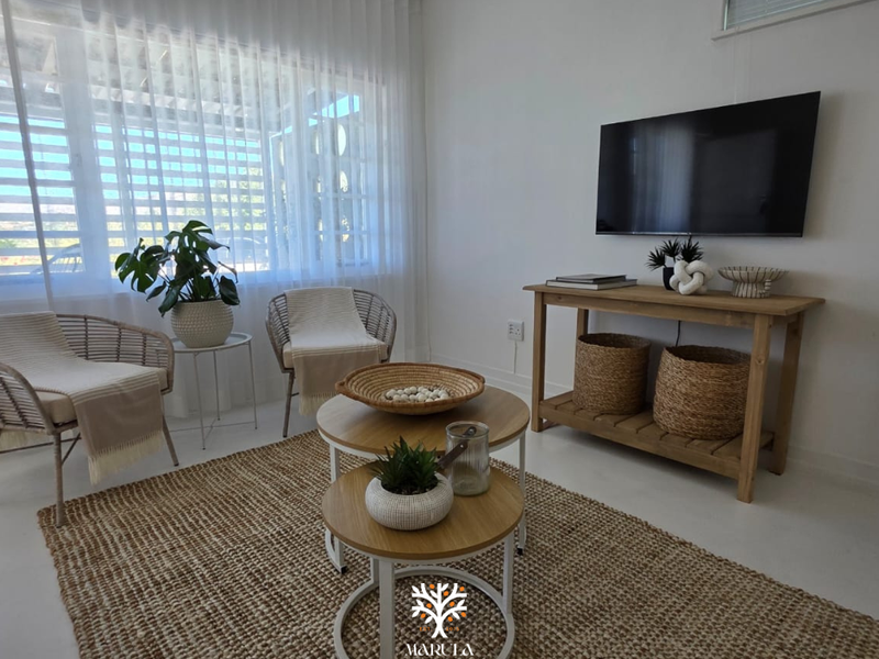A bright and airy living room featuring large windows with sheer curtains and a wall-mounted television, creating a comfortable and inviting space.