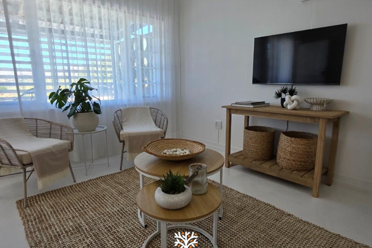 A bright and airy living room featuring large windows with sheer curtains and a wall-mounted television, creating a comfortable and inviting space.