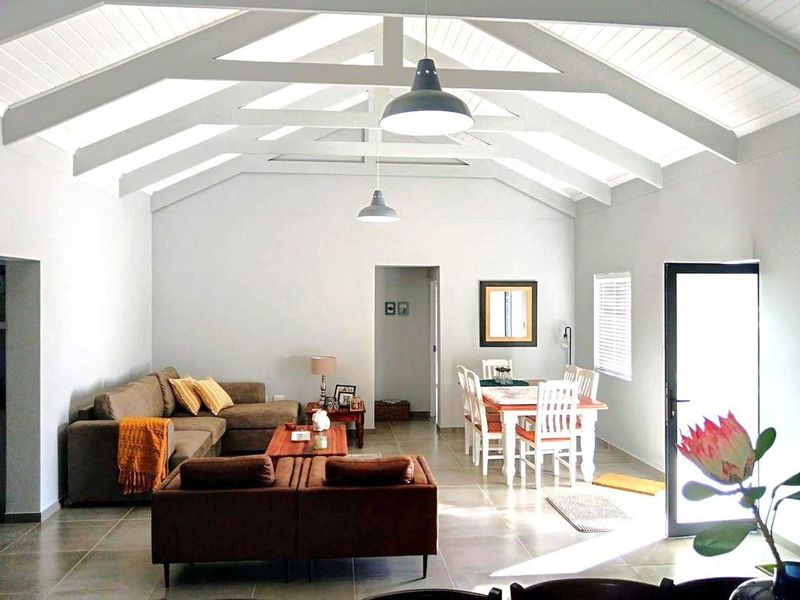 Spacious open-plan living and dining area featuring a high vaulted ceiling with exposed beams, tiled floors, and abundant natural light.