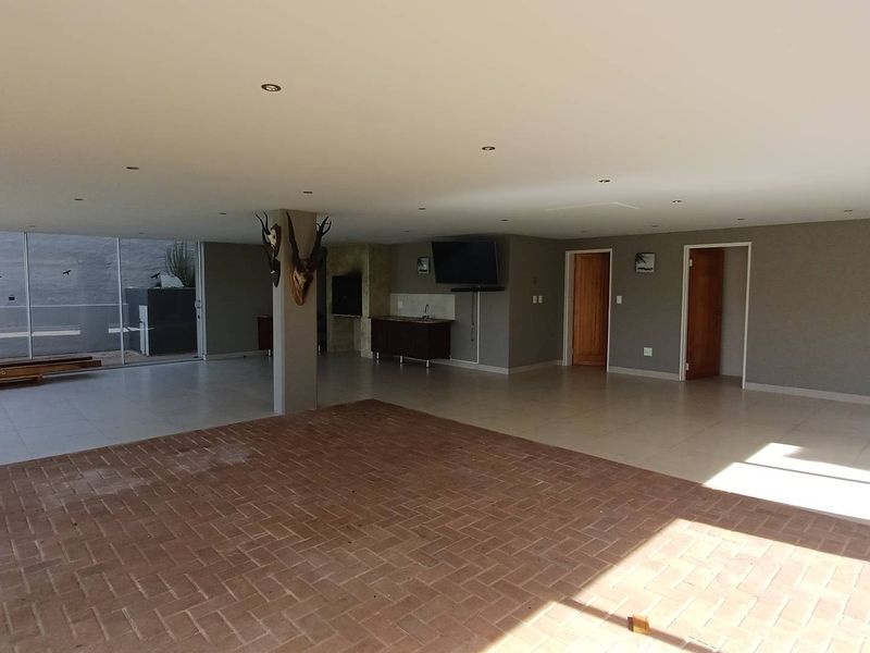 Spacious open-plan living area featuring a built-in braai, kitchenette, recessed lighting, and a combination of tiled and brick flooring with access to the outdoors.