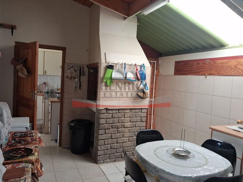 Covered patio area featuring a built-in braai, tiled flooring, and exposed timber rafters with translucent roof sheeting, providing a functional outdoor entertainment space.