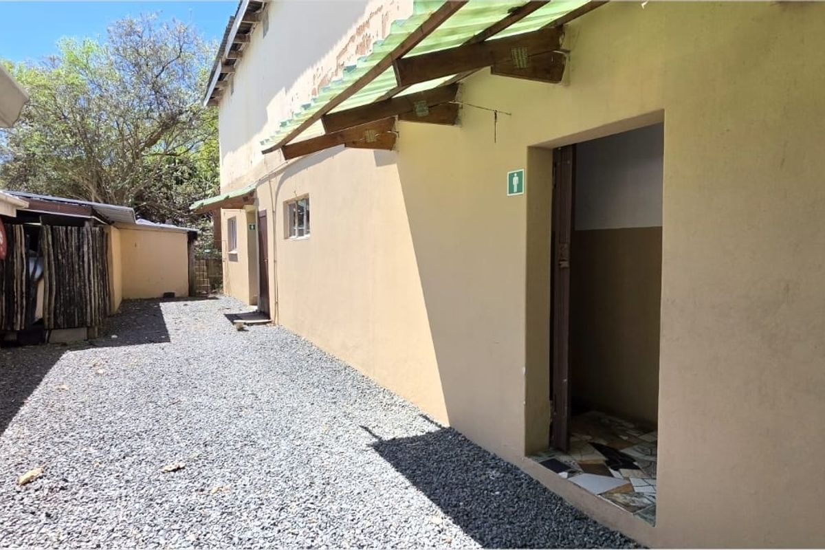 Rear exterior area featuring a gravel pathway, external access doors, and a protective awning structure along the building facade.