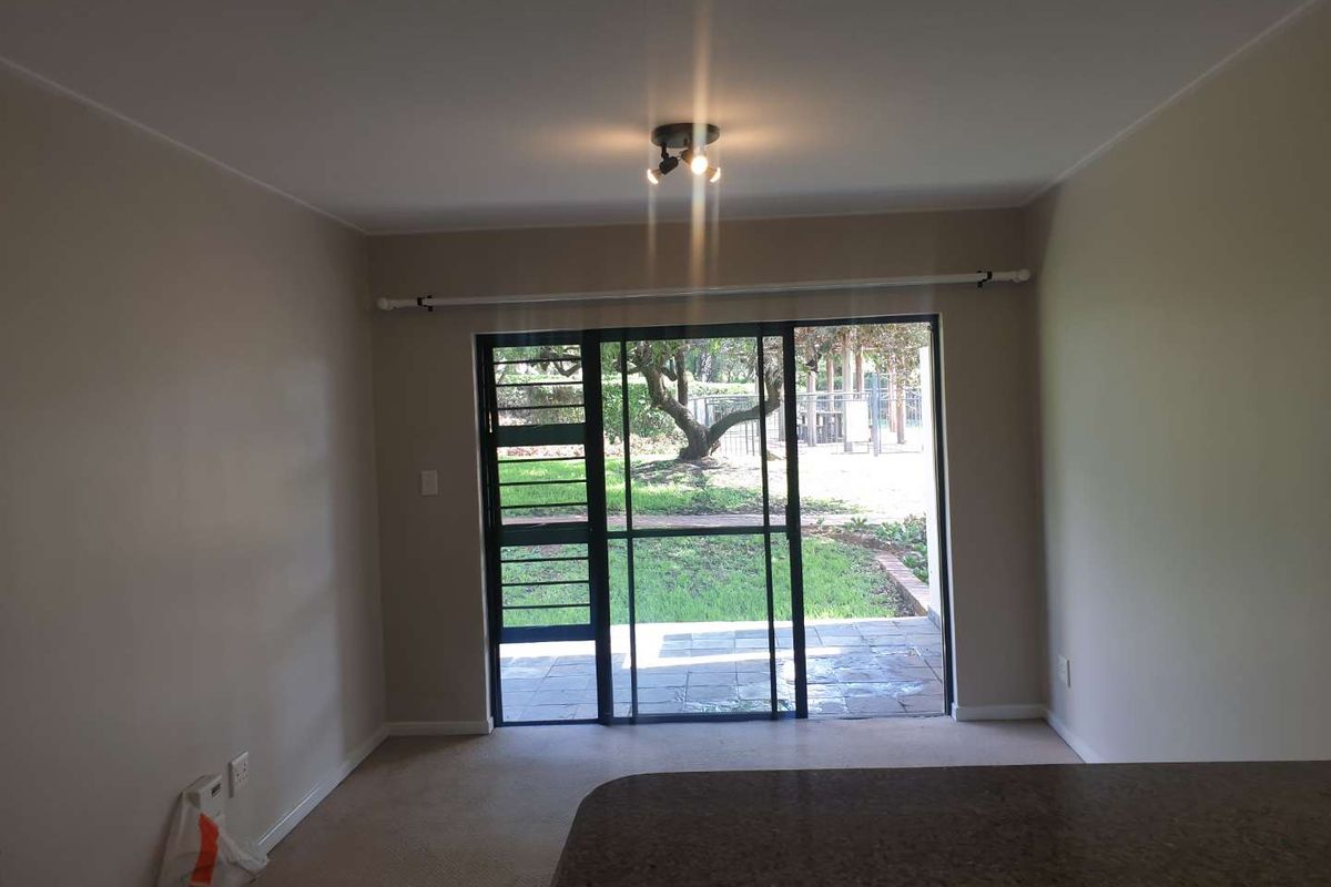 An empty living room featuring neutral walls, carpeted flooring, and a sliding glass door with a security gate leading to an outdoor patio area.