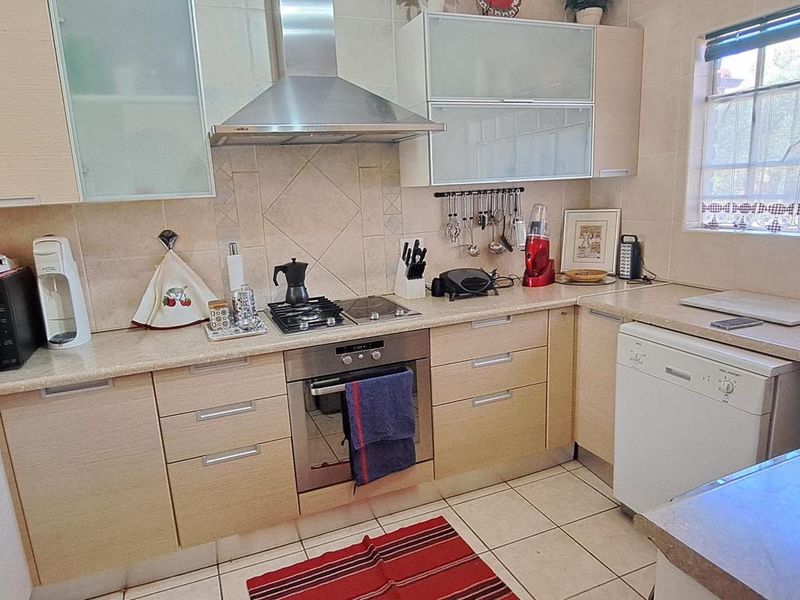 A functional kitchen featuring light wood cabinetry, a stainless steel extractor fan, gas hob, built-in oven, and tiled finishes throughout.