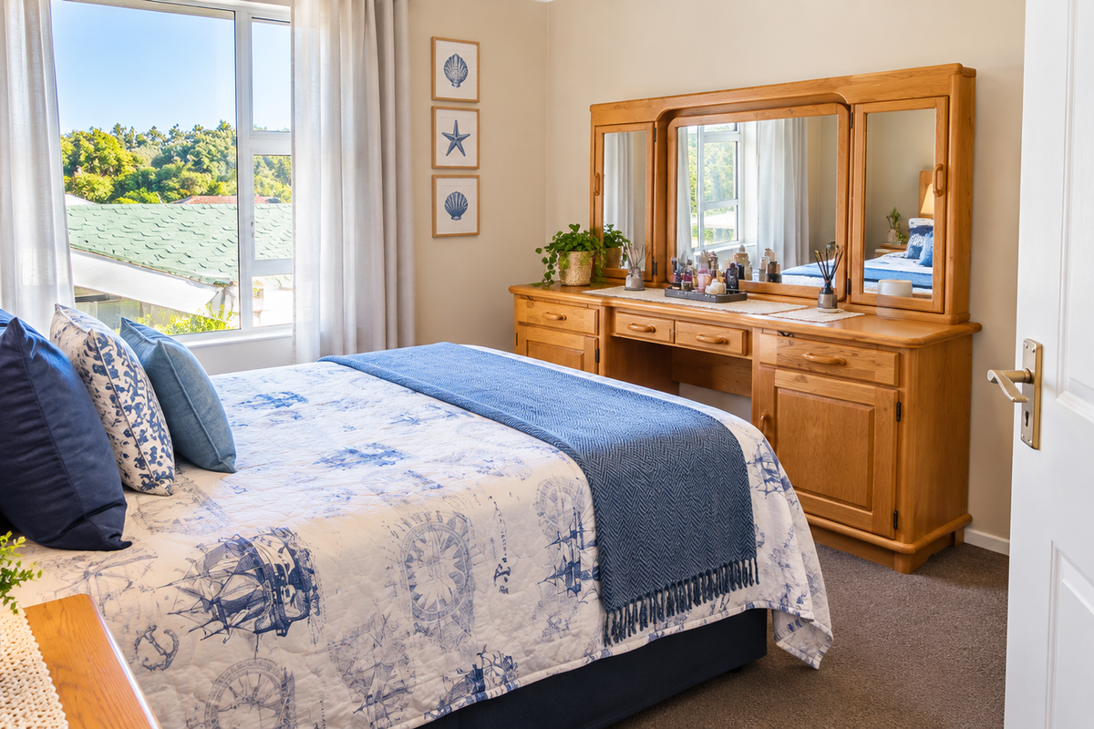 A well-lit bedroom featuring neutral walls, carpeted flooring, and a large window providing natural light and an exterior view.