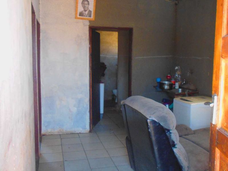 A basic living area featuring tiled flooring and exposed roof structure, requiring significant cosmetic updates and wall finishing to improve the overall condition.
