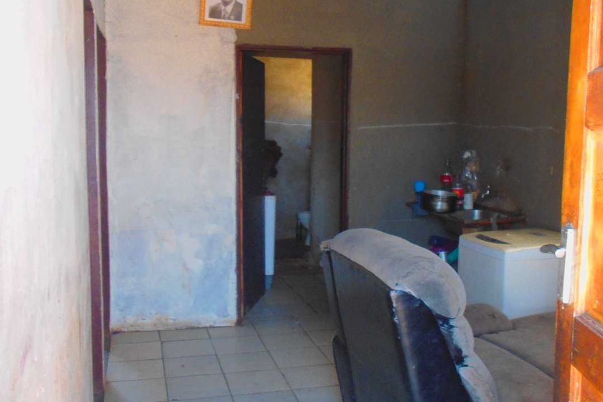 A basic living area featuring tiled flooring and exposed roof structure, requiring significant cosmetic updates and wall finishing to improve the overall condition.