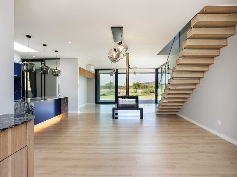 Modern open-plan living area featuring a striking floating timber staircase, central fireplace, and a sleek kitchen with stone countertops and integrated lighting.