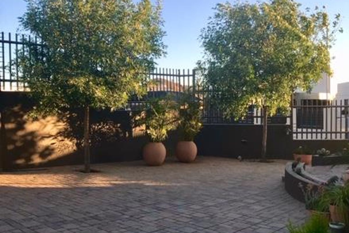 A well-maintained paved courtyard area featuring perimeter metal fencing and established trees, providing a private and low-maintenance outdoor space.