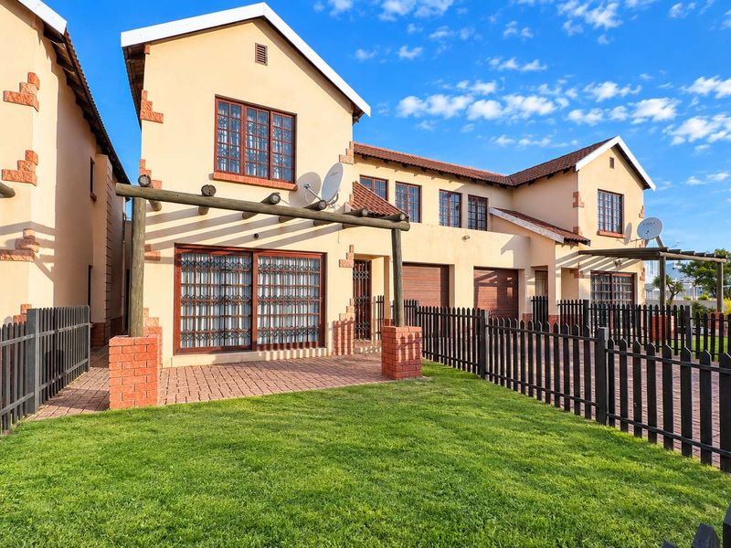Rear view of a townhouse featuring a private garden, brick-paved patio with a timber pergola, and secure perimeter fencing.