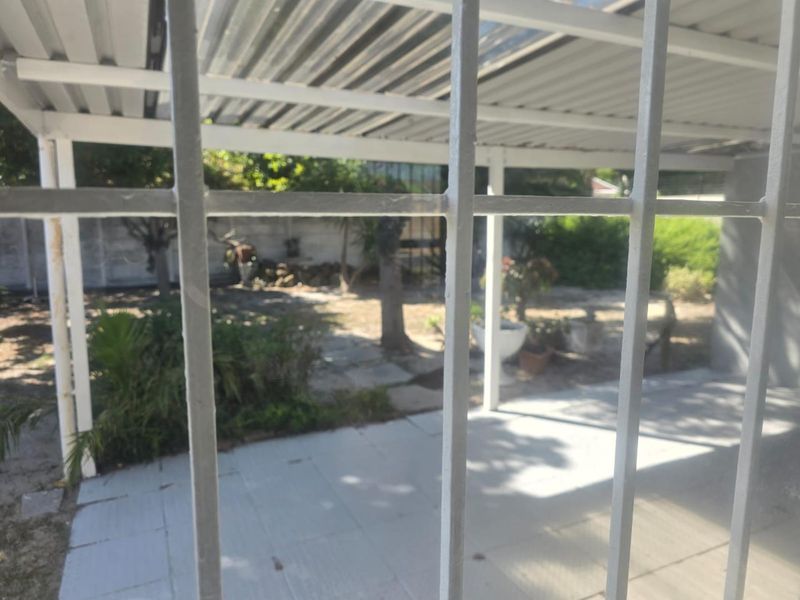 A covered outdoor patio area featuring tiled flooring and a corrugated metal roof, overlooking a rear garden space.