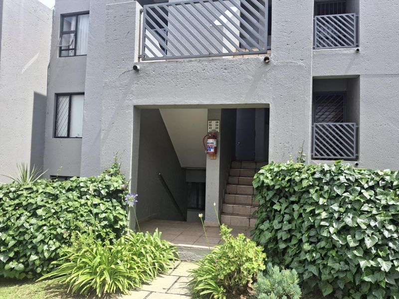 Exterior view of an apartment complex entrance featuring a concrete staircase, metal balustrades, and landscaped garden beds.