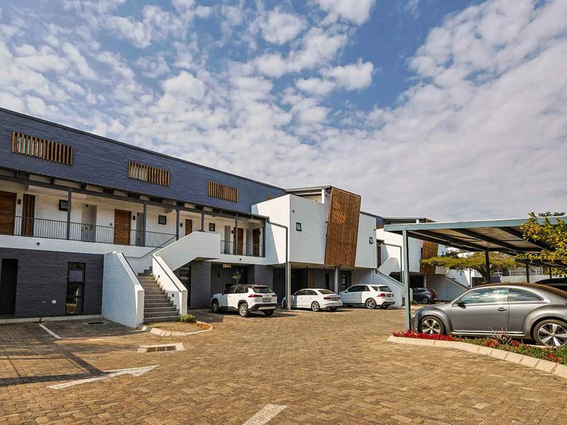Exterior view of a modern apartment complex featuring paved parking, covered carports, and a multi-level facade with timber accents and external staircases.